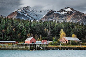Cannery located in bay of Pacific Ocean is a part of famous fishing village Haines in Alaska in background with mountains and glaciers covered with snow during warm autumn sunny day