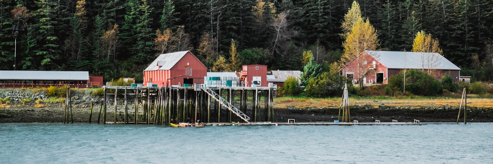 Cannery located in bay of Pacific Ocean is a part of famous fishing village Haines in Alaska in background with mountains and glaciers covered with snow during warm autumn sunny day