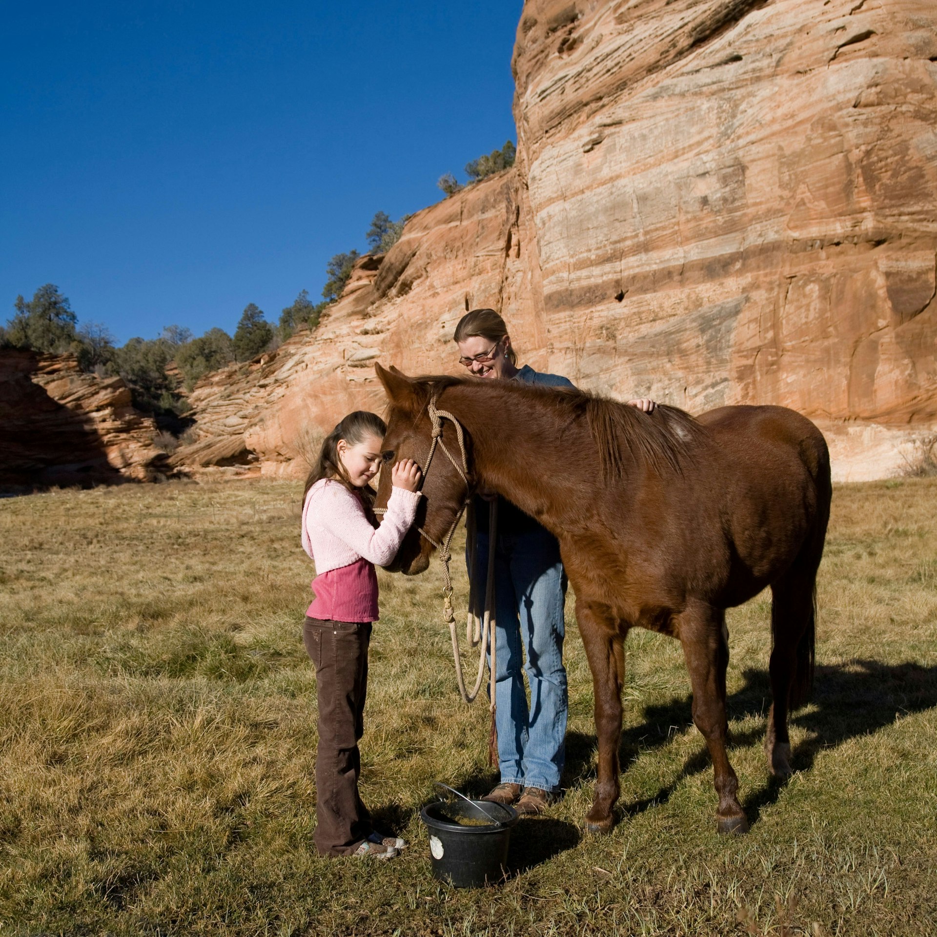 A girl feeds a horse in front of a rock formation and a bright blue sky at Best Friends Animal Sanctuary, Utah