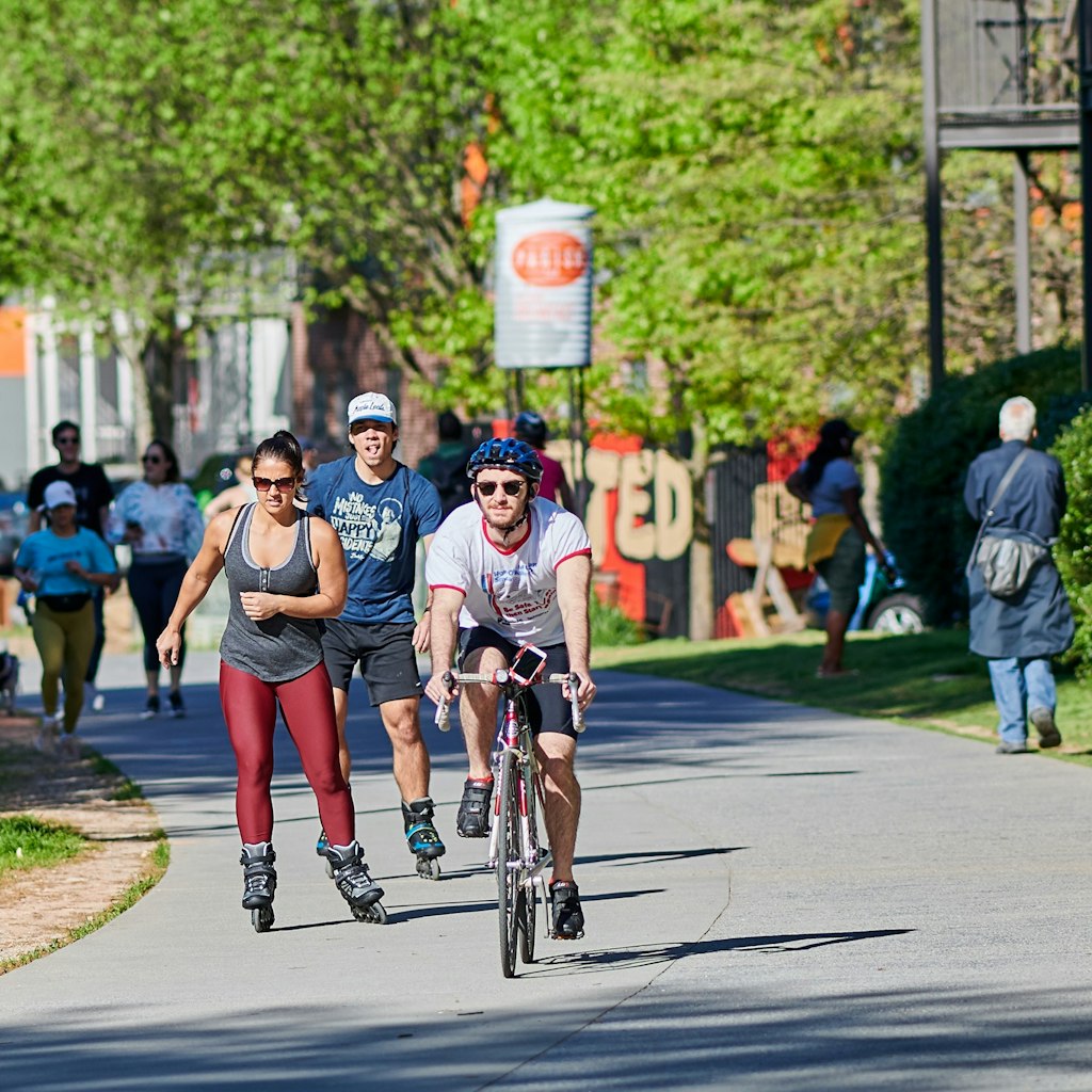 A group of people bike, roller blade and walk down the paved Atlanta Beltline.