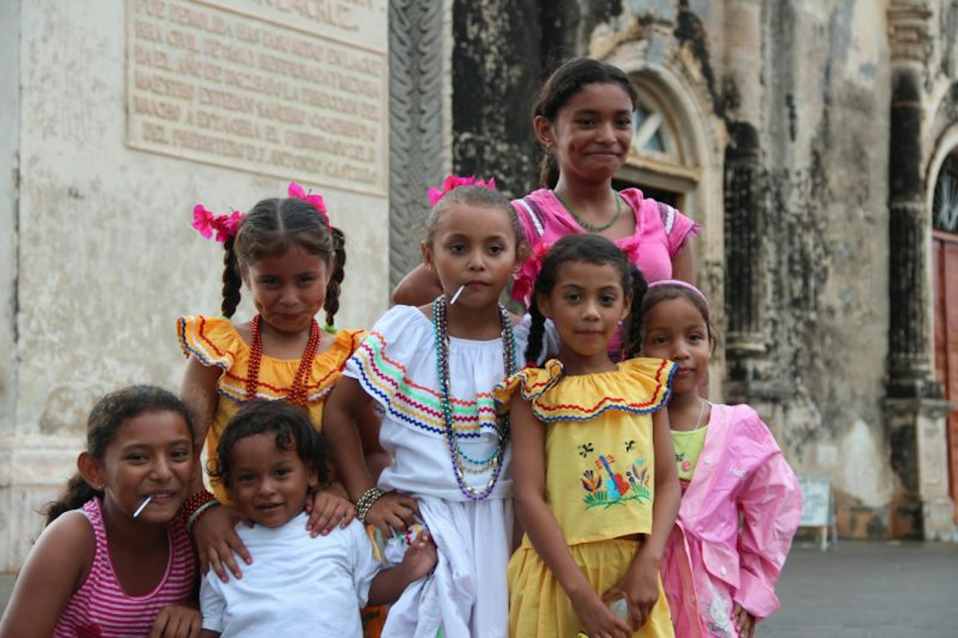 A group of girls in colorful outfits smiling in front a church in Granada, Nicaragua