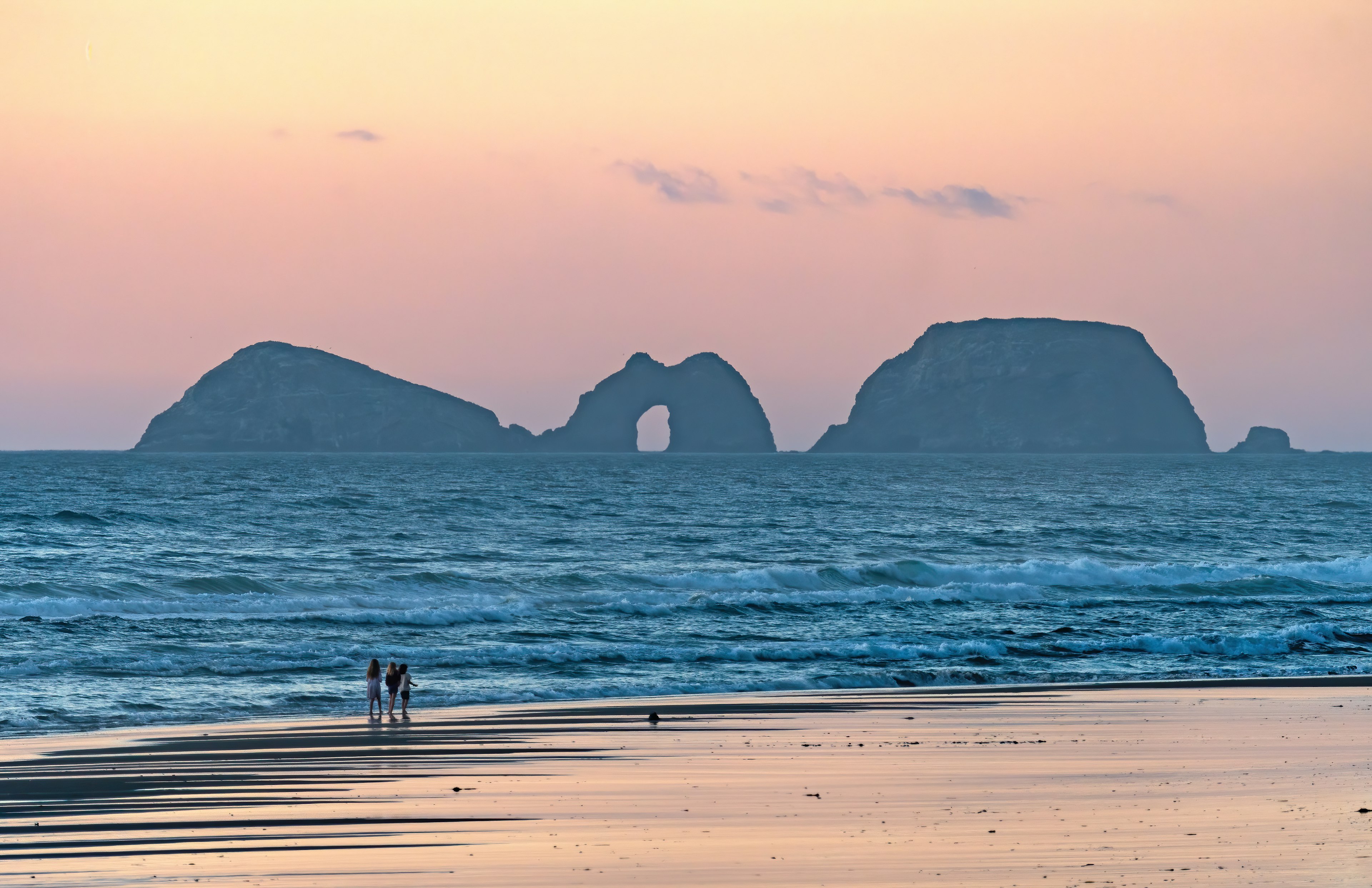 A group of people walk along the ocean coast at Cape Lookout State Park in Oregon at twilight.