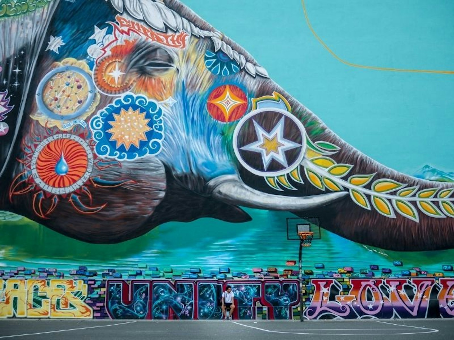 Massive colorful mural of an elephant with tusks holding a ballon in the shape of the earth in its trunk