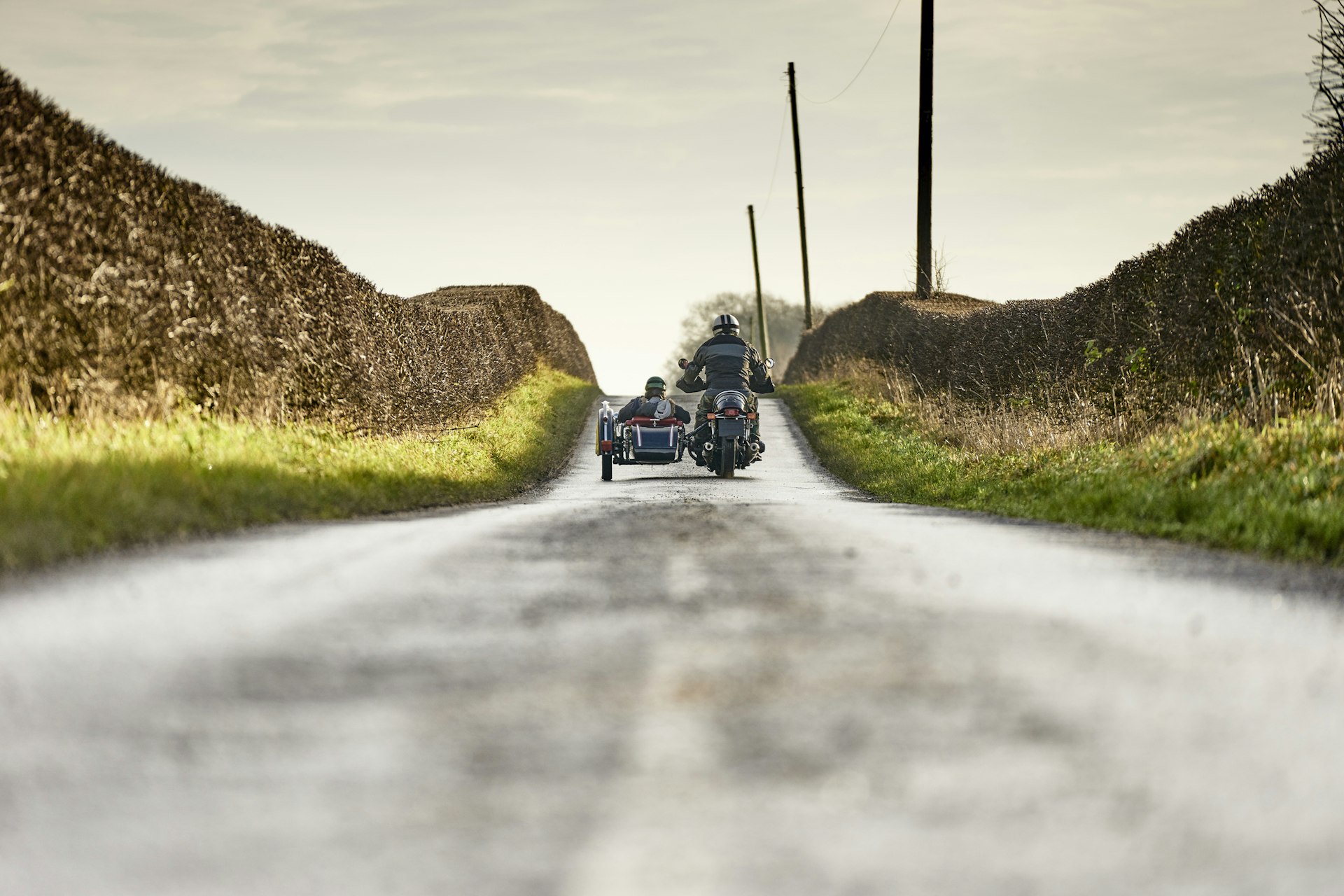 Rear view of senior man and grandson riding motorcycle and sidecar on rural road