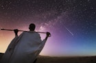 Ethiopia. Rear view of a senior ethiopian man carrying his stick over his shoulder and watching the milky way in a starry sky.