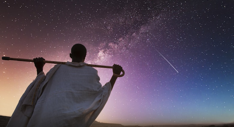 Ethiopia. Rear view of a senior ethiopian man carrying his stick over his shoulder and watching the milky way in a starry sky.