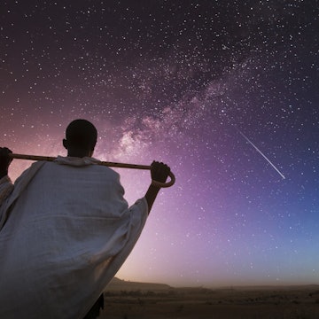 Ethiopia. Rear view of a senior ethiopian man carrying his stick over his shoulder and watching the milky way in a starry sky.