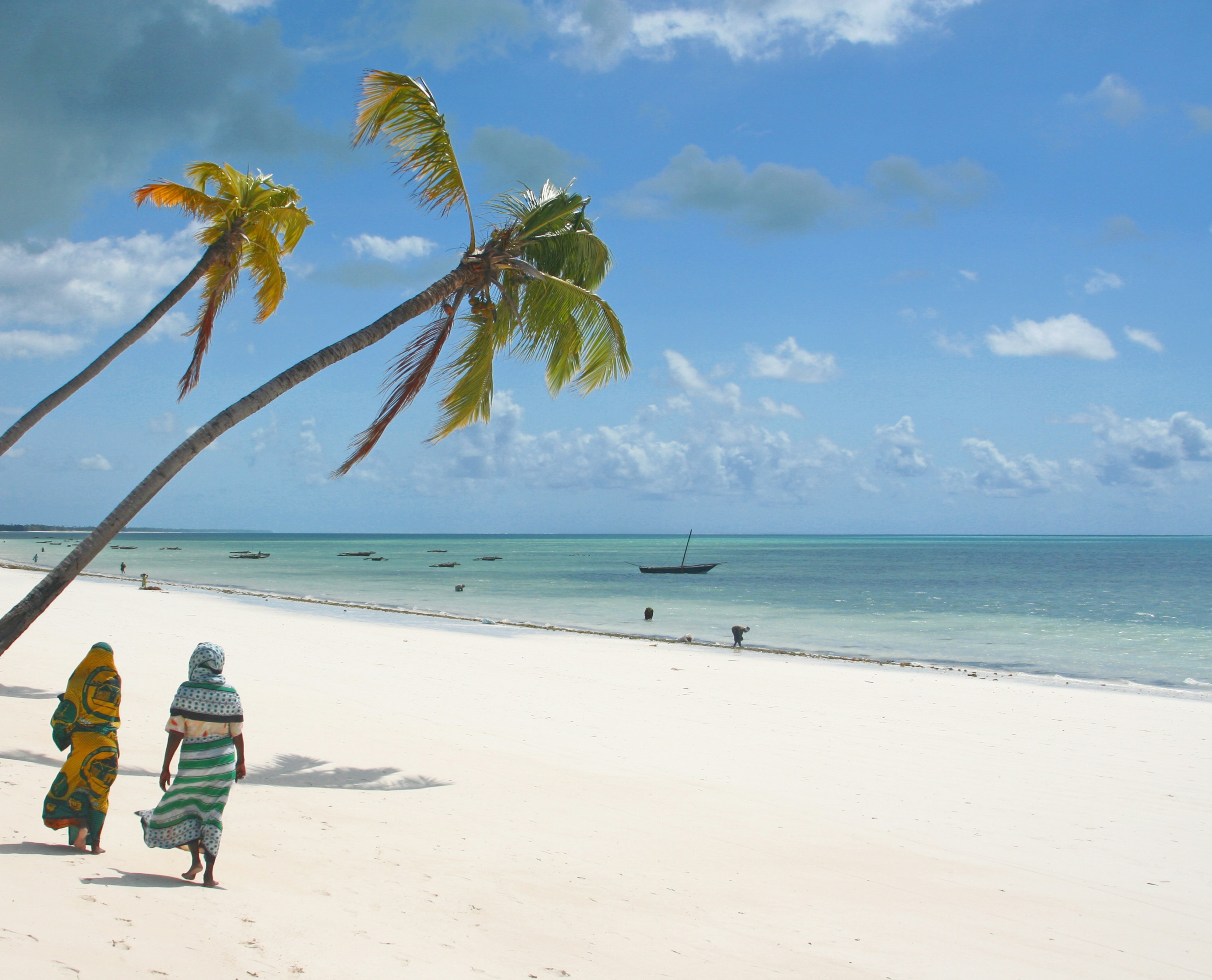 African women walk on the beach under palms on Zanzibar Island