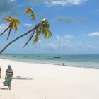 African women walk on the beach under palms on Zanzibar Island