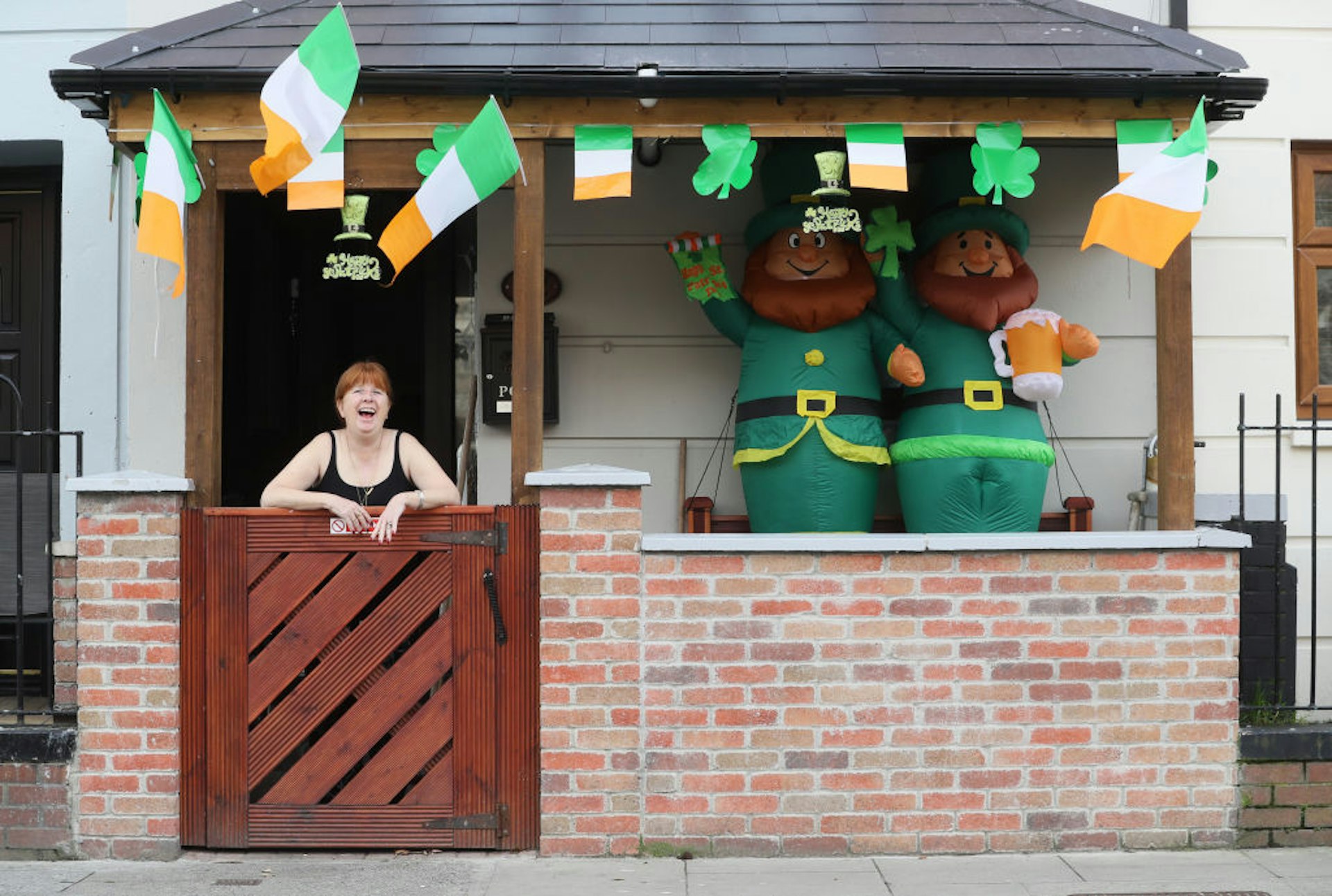 Женщина возле своего дома на Ориэл-стрит в Дублине, украшенного в честь Дня Святого Патрика флагами и двумя надувными гномами.