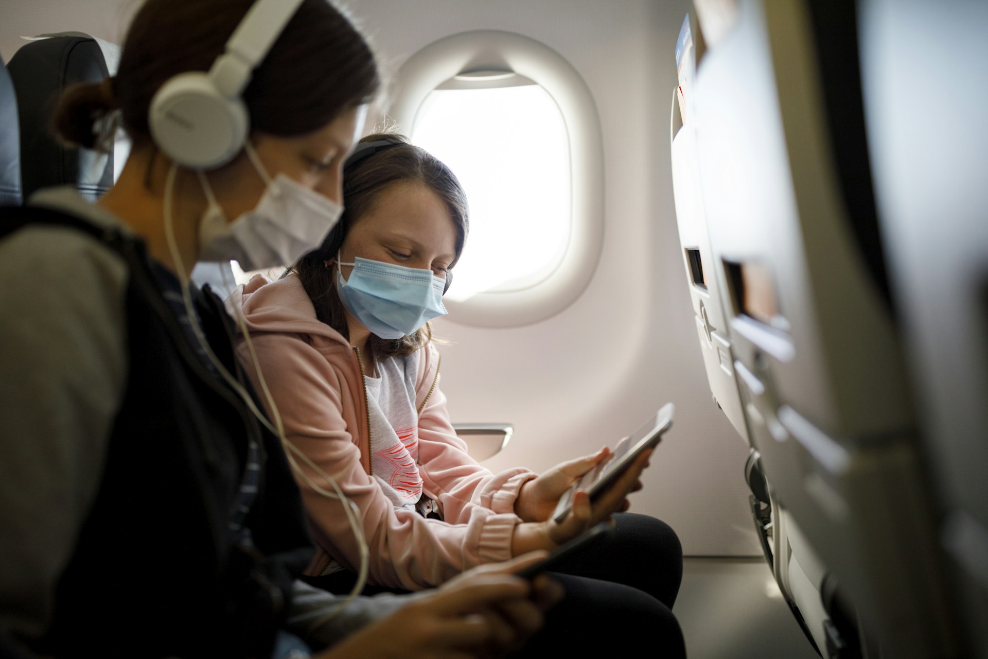 A mother and child wear face masks on an airplane