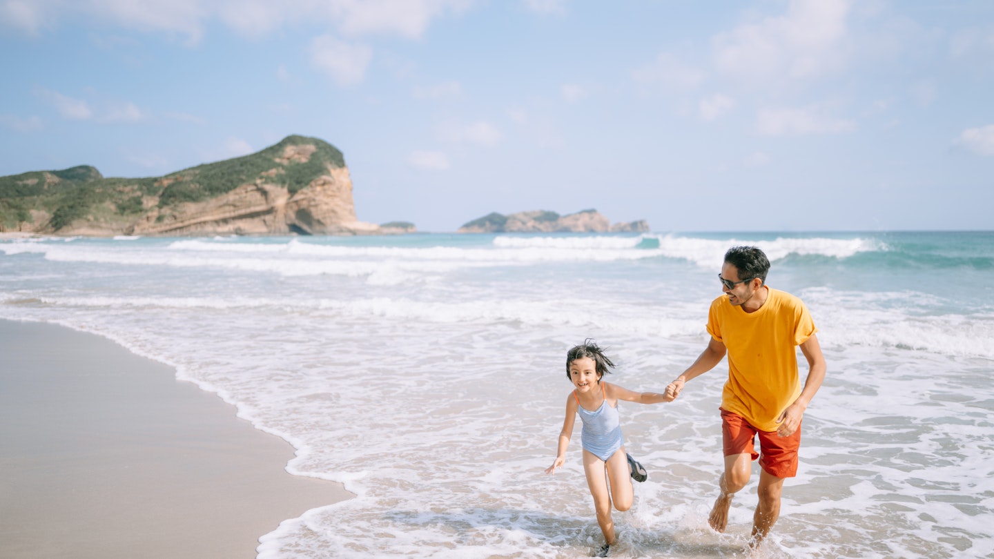Japanese father and his young daughter playing in waves on beach, Tanegashima Island