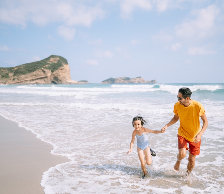 Japanese father and his young daughter playing in waves on beach, Tanegashima Island