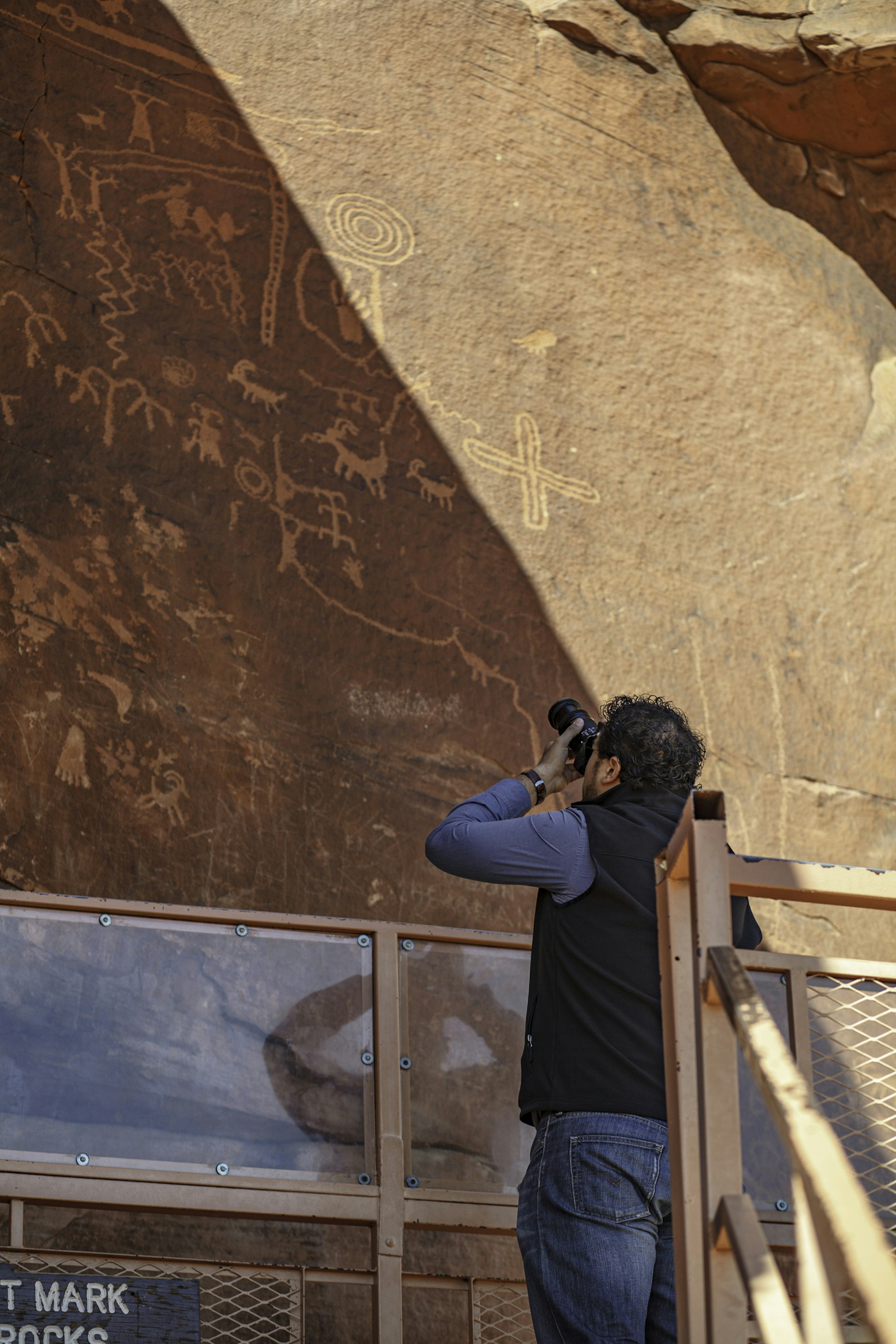 A man is photographing a famous rock full of Petroglyphs Cave Paintings