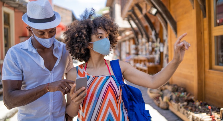 Afro Couple wearing protective face mask and walking on the street while using smart phone for navigation
