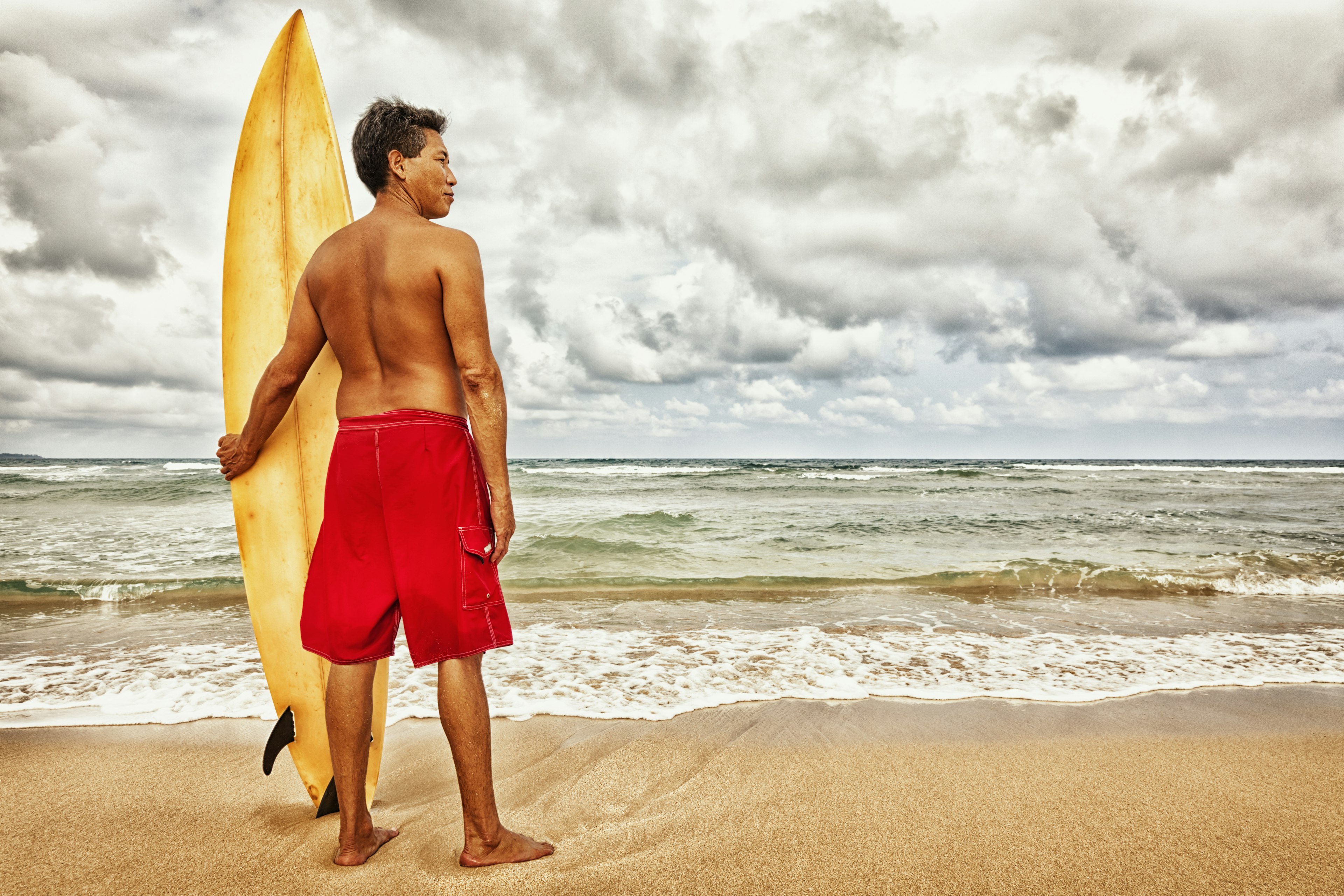 A Hawaiian surfer standing with his board on a Kauai beach