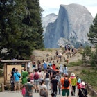 Tourists walk to Glacier Point with a background view of Half Dome at Yosemite National Park. 