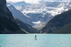 woman paddleboards across mountain lake
