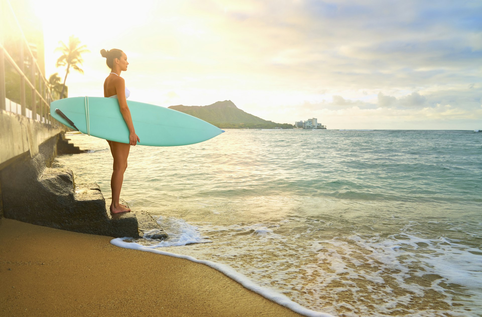 Pacific Islander woman holding surfboard on staircase at ocean