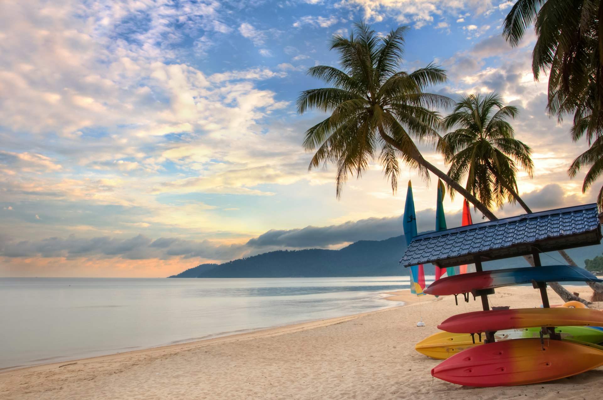 A deserted beach with palms and stored boats on Tioman Island, as the sunrise creates pink and light-blue light