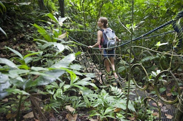 A female hiker crossing a hanging bridge in the dense jungle near Quepos, Puntarenas Province.