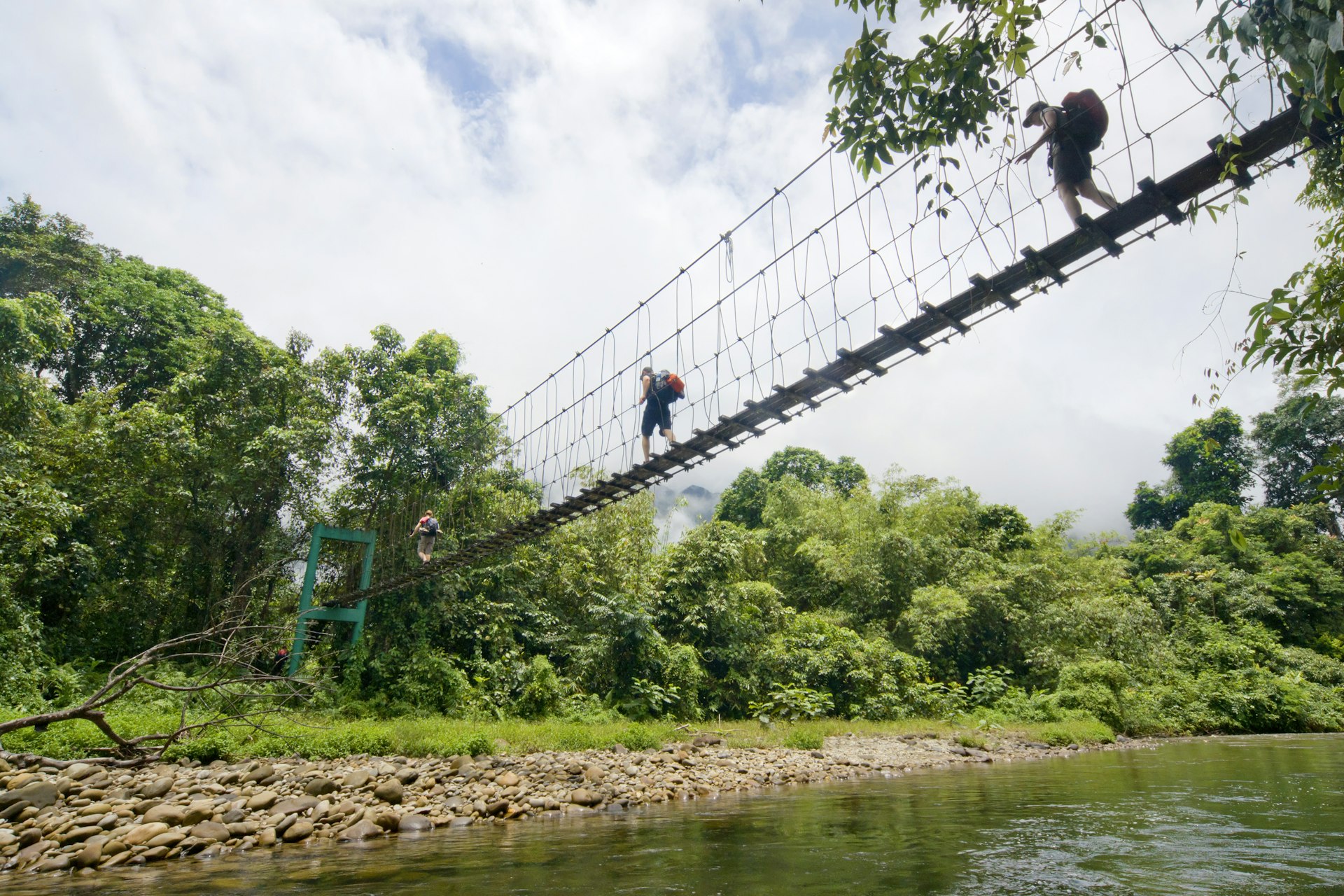 Two tourists with backpacks crossing a suspension bridge.