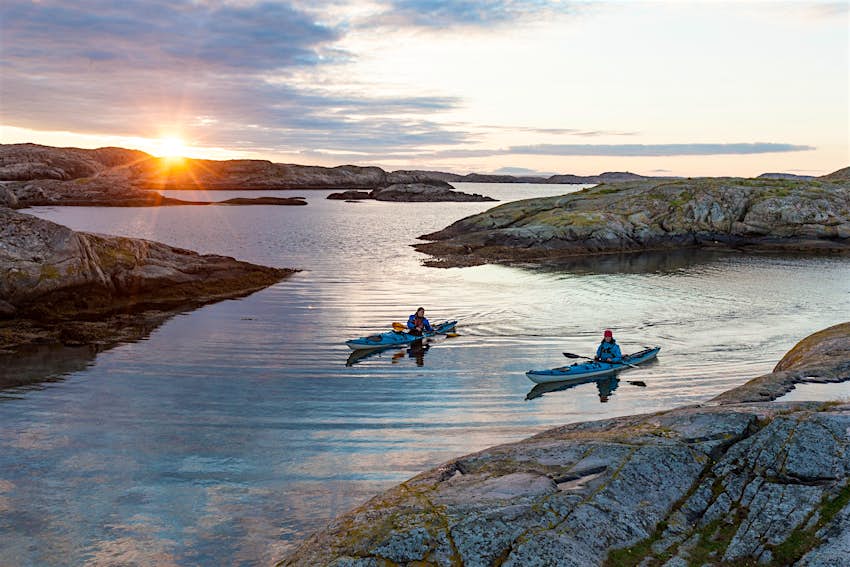 Two sea kayakers paddle in a rocky bay at sunset