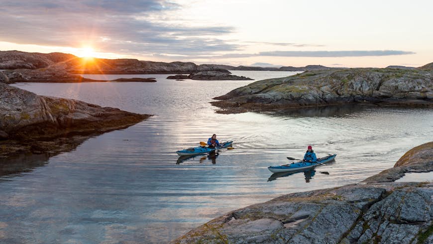 Two sea kayakers paddle in a rocky inlet at sunset