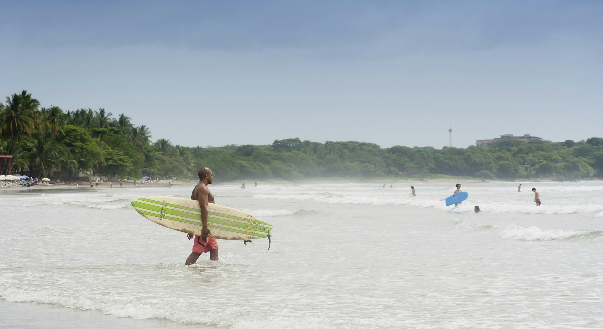 A surfer wades out to join other surfers in the water