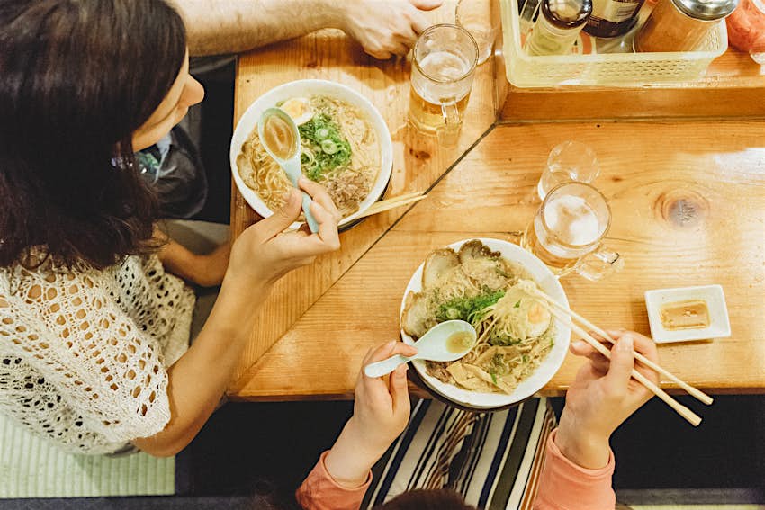 Aerial shot of two friends tucking into bowls of noodles in a restaurant