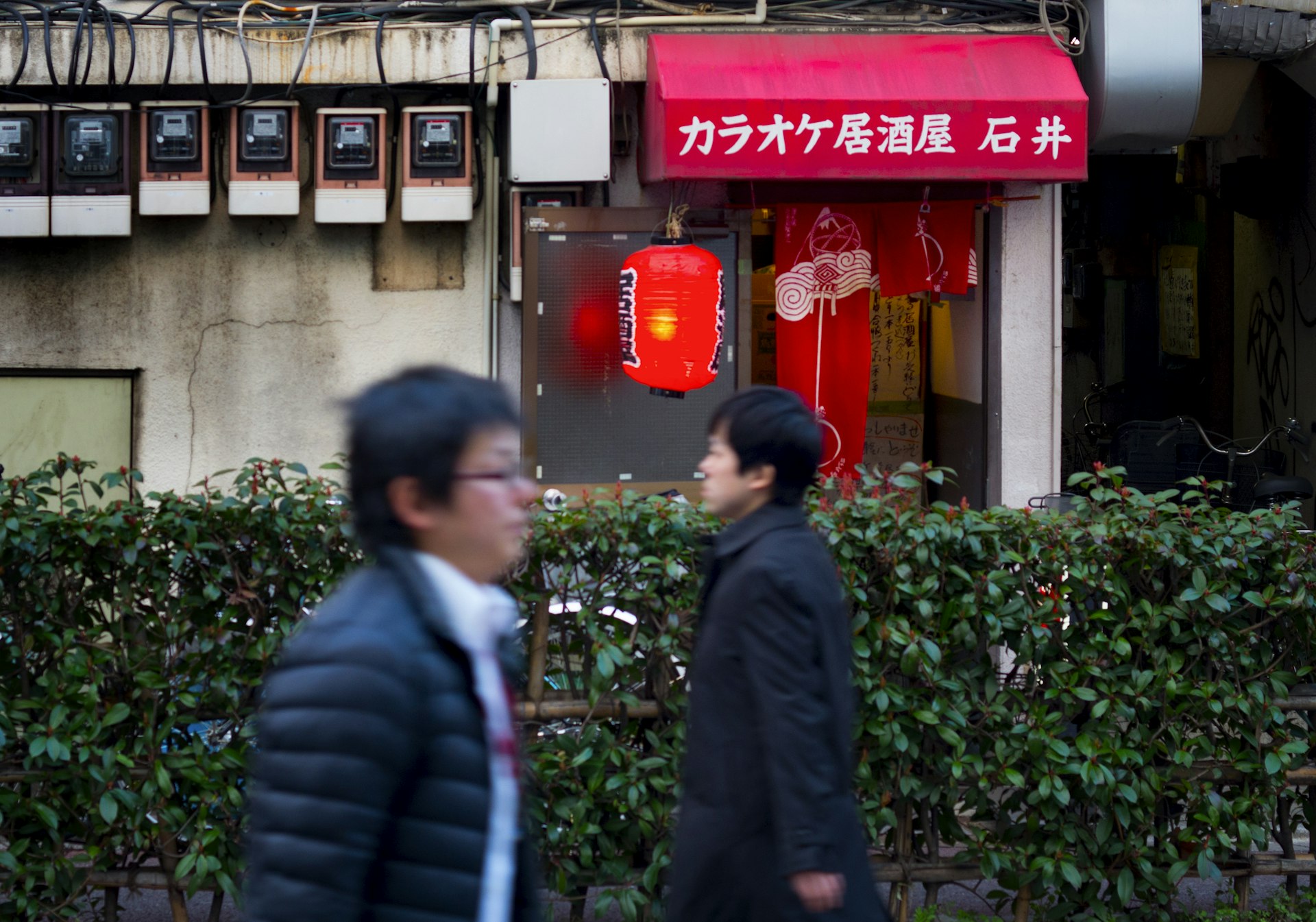 Two men walking in opposite directions past a karaoke bar near the Kita-Senju train station in Northern Tokyo