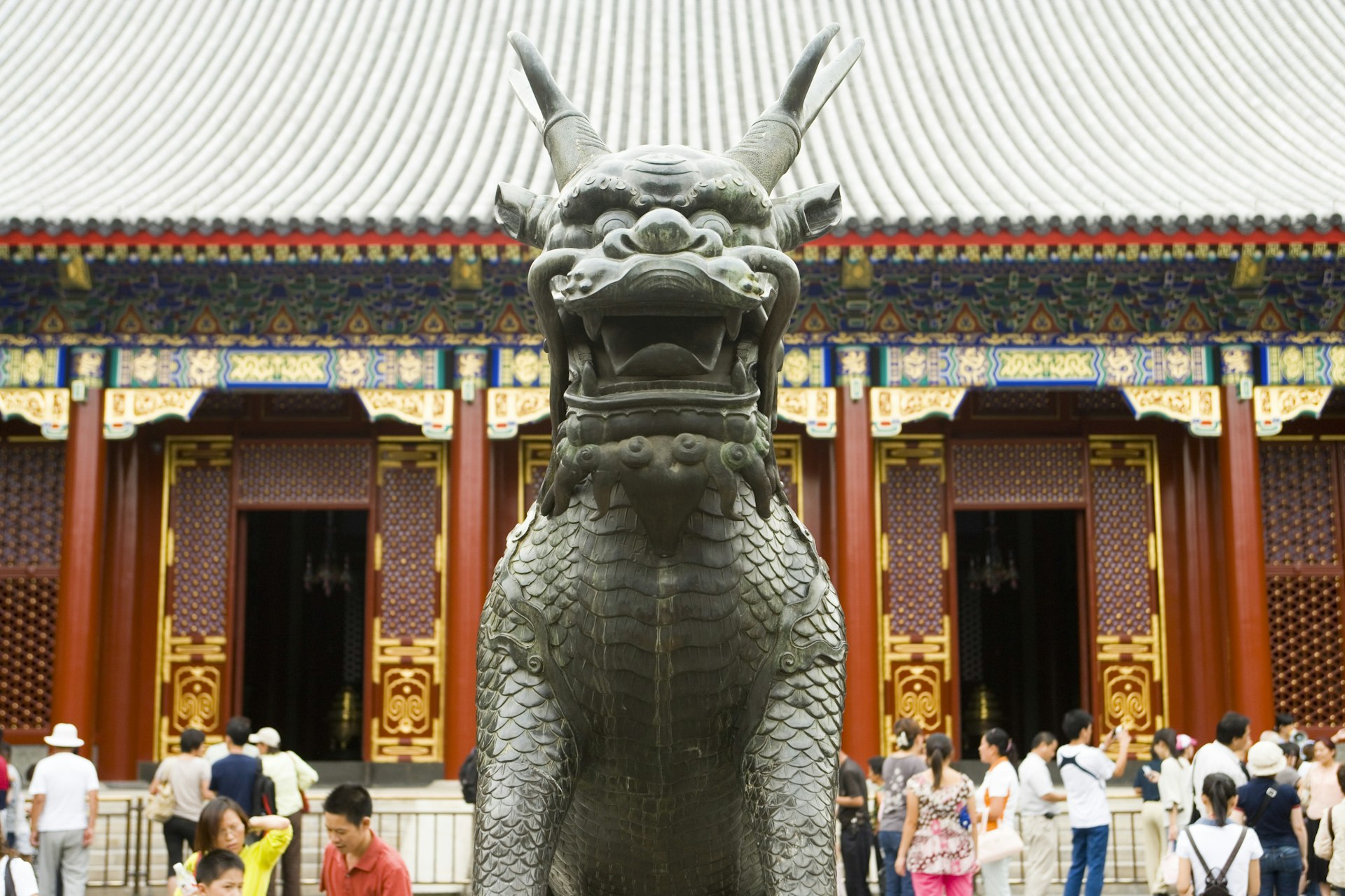 A sculpture of a fierce, horned dragon mid-road in front of crowds visiting the Summer Palace