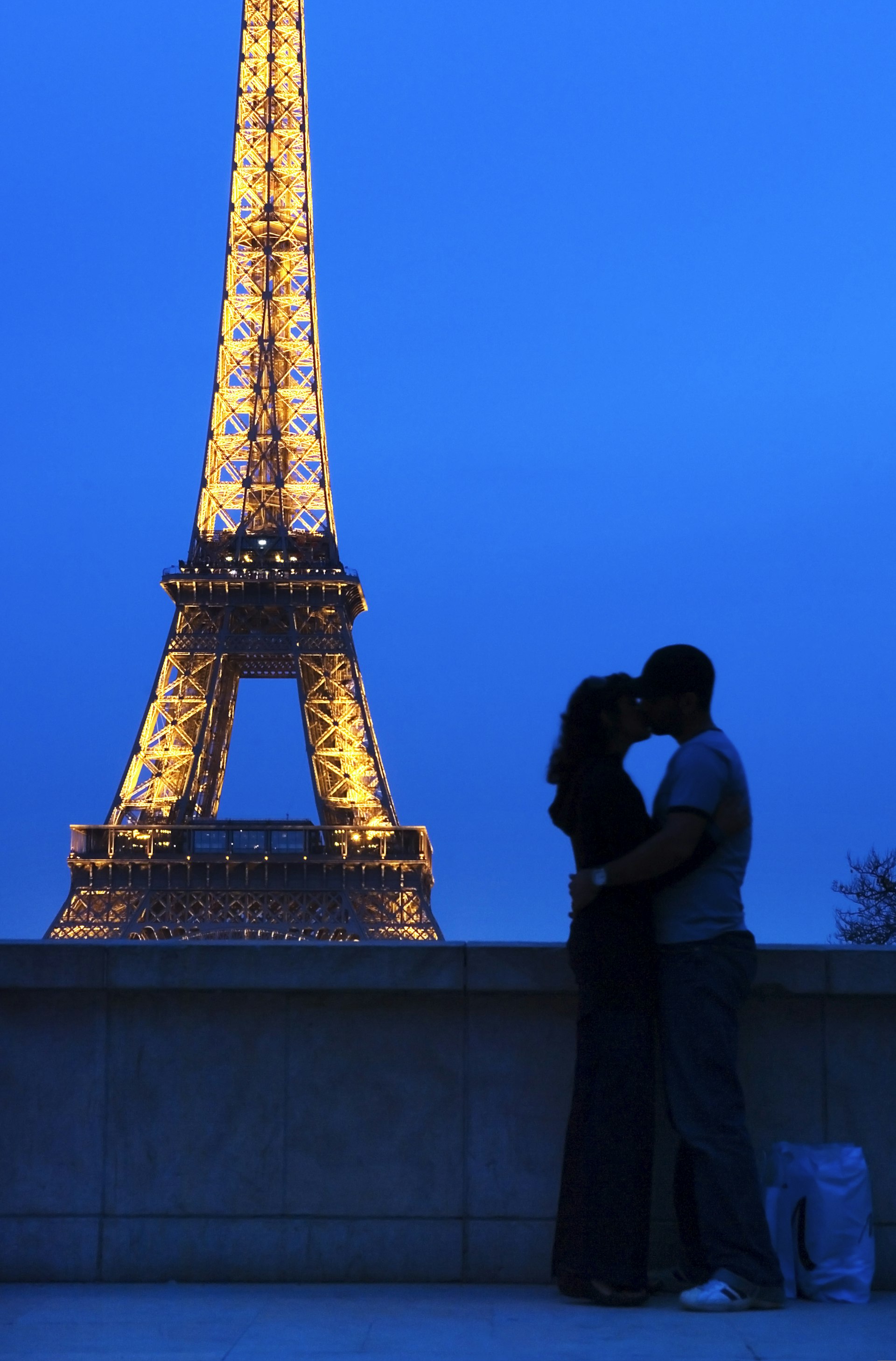 A couple embracing in front of the Eiffel Tower at night. 