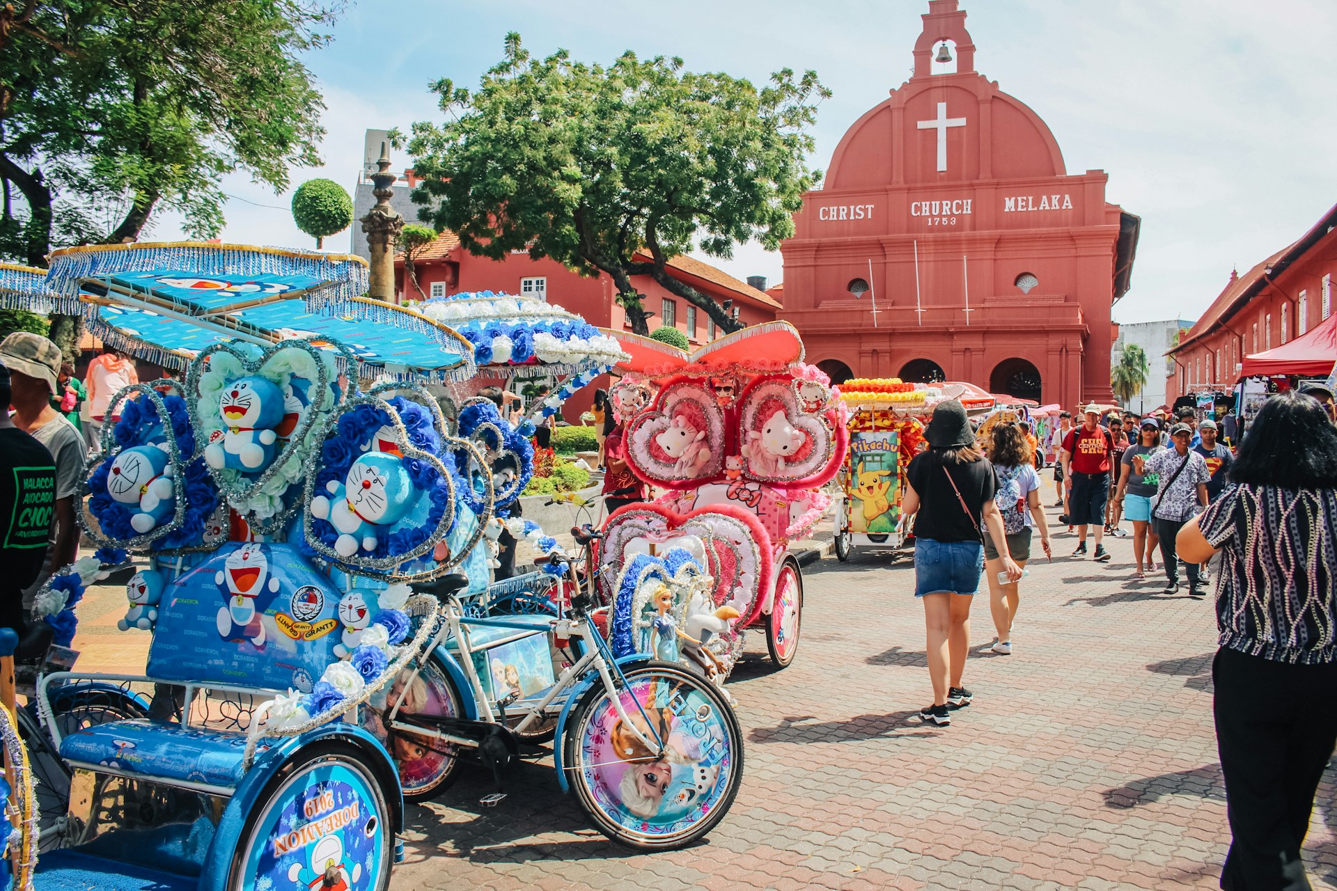 A row of colorful four-wheel cycles stand in a main square backed by a large church building painted red
