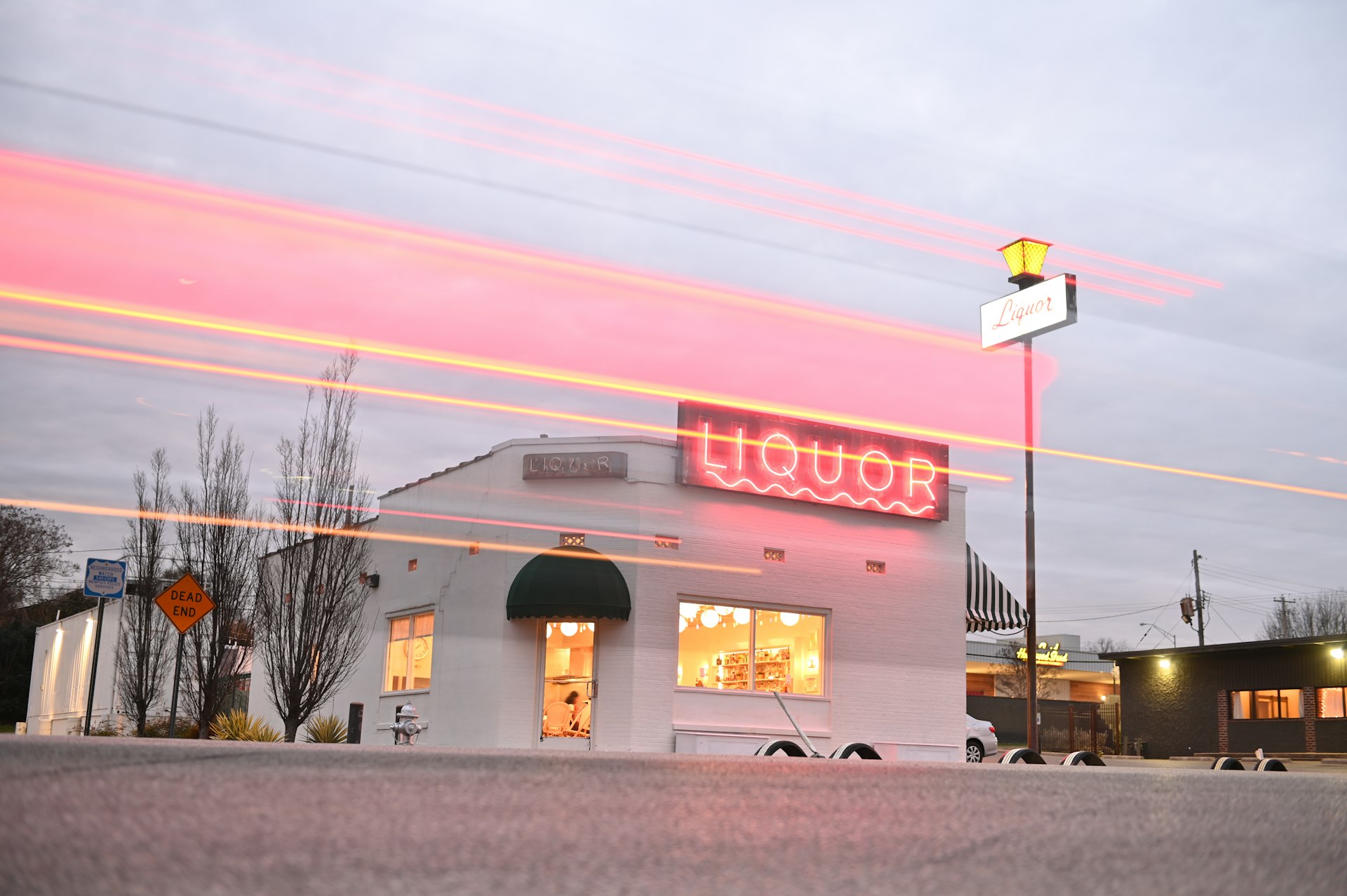 A low-rise white brick building with a huge pink neon sign spelling "liquor"