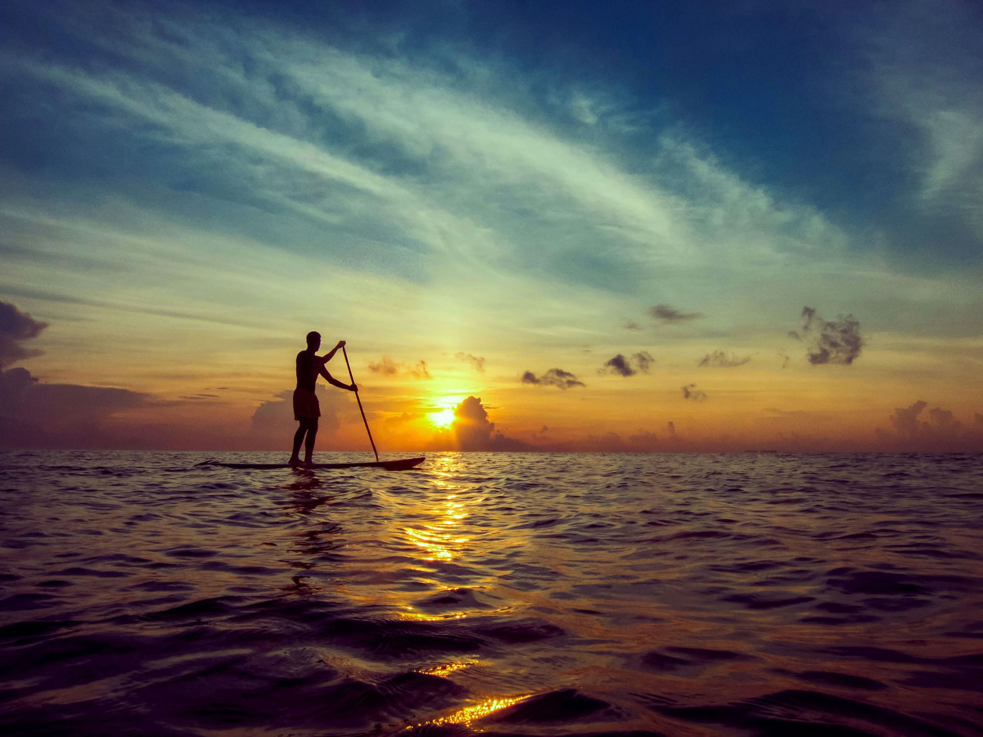 A young man in silhouette, stand-up paddleboarding during a beautiful sunrise