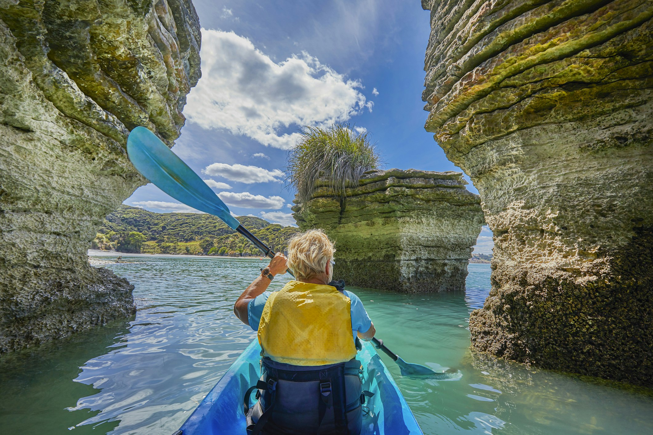 Woman paddling Kayak around the rock formations know as the Pancake Rocks on the west coastline at the town of Raglan, popular for leisure kayakers and paddleborders,Raglan,Waikato,North Island,New Zealand