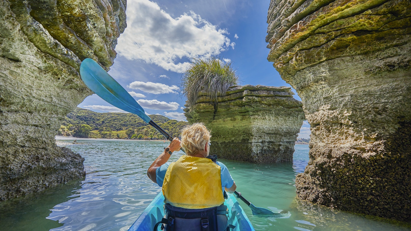 Woman paddling Kayak around the rock formations know as the Pancake Rocks on the west coastline at the town of Raglan, popular for leisure kayakers and paddleborders,Raglan,Waikato,North Island,New Zealand