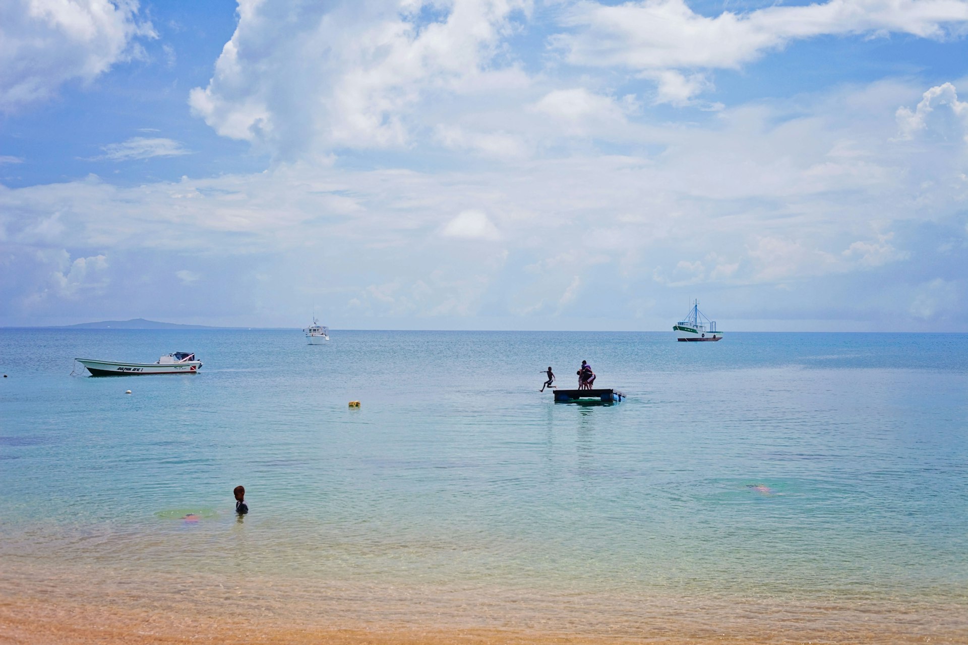 Looking out into the water as people and boats rest and play in the clear tropical water. Big Corn Island is seen on the horizon. 