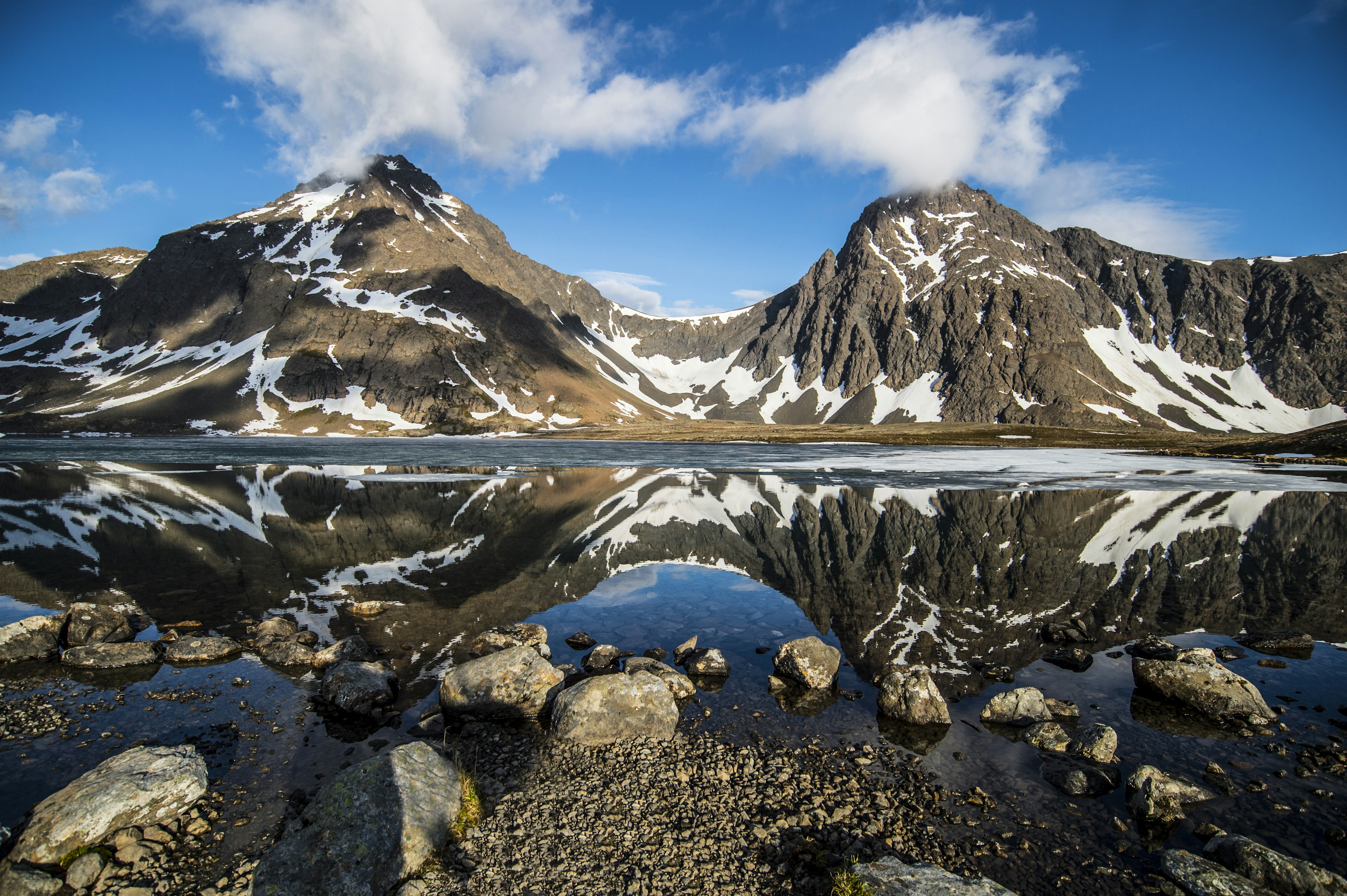 Snow-streaked mountains under a blue sky, with a lakeshore in the foreground