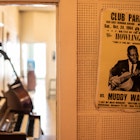 An old concert poster for a Howlin Wolf show hangs on a white wall. In the background you can see an piano and a bass. 
