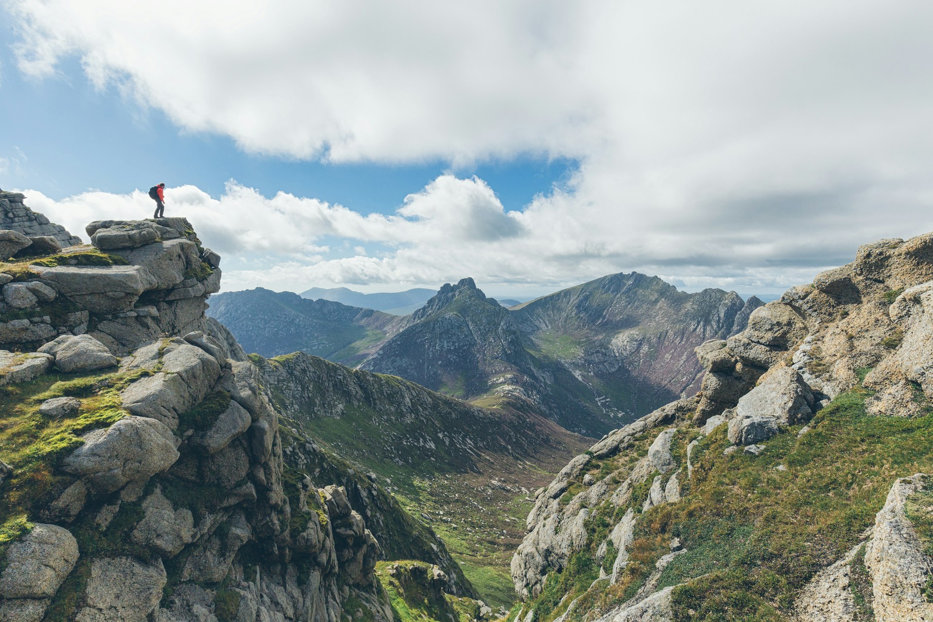 A hiker stands on a mountain summit looking out over a valley