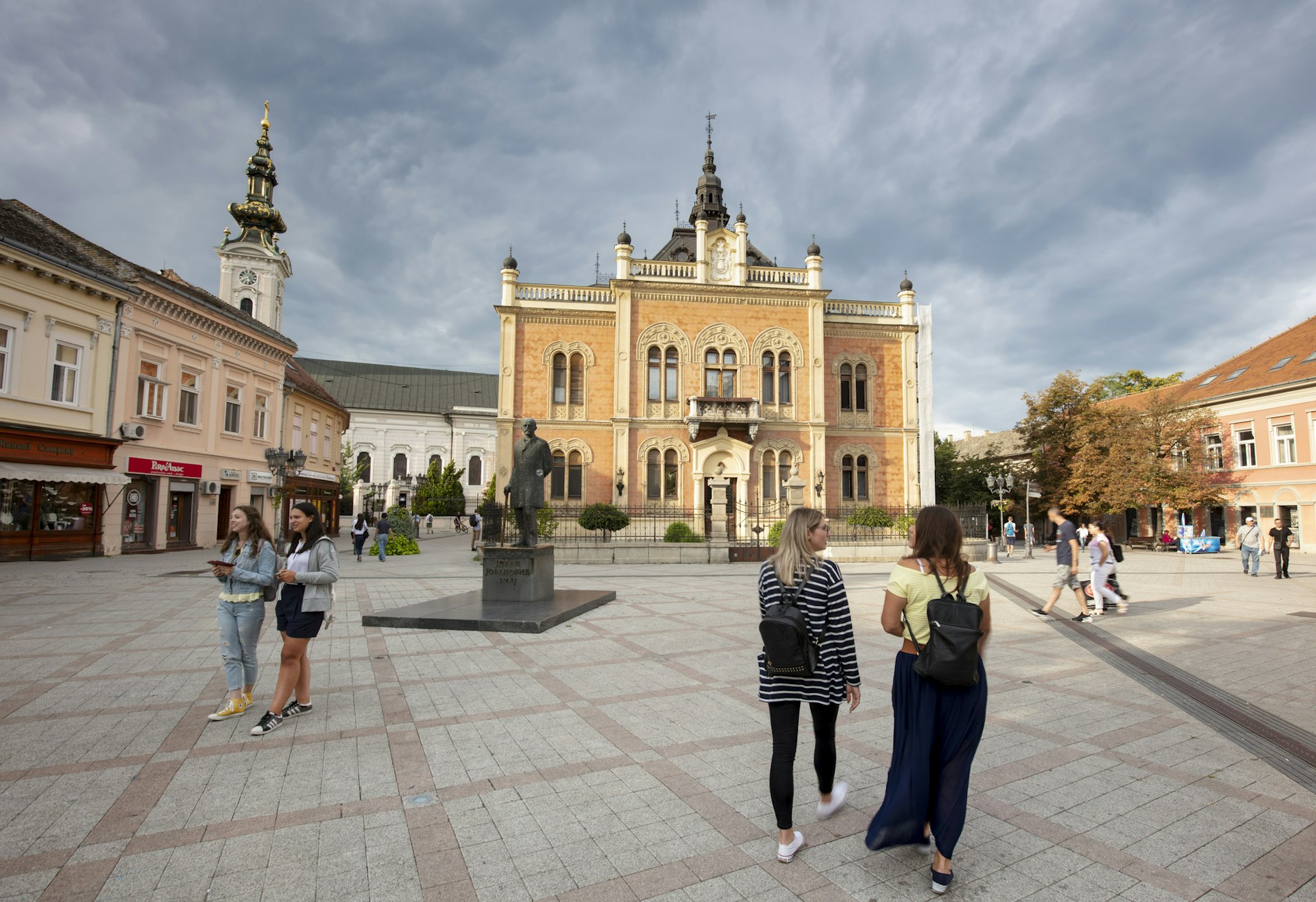 People walk across a square in front of a Baroque church building