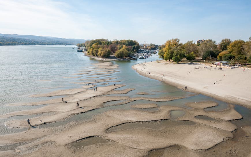 Lågvatten i Donau med silhuetter av människor som går på sandöarna kvar efter vattenavdrag i Novi Sad