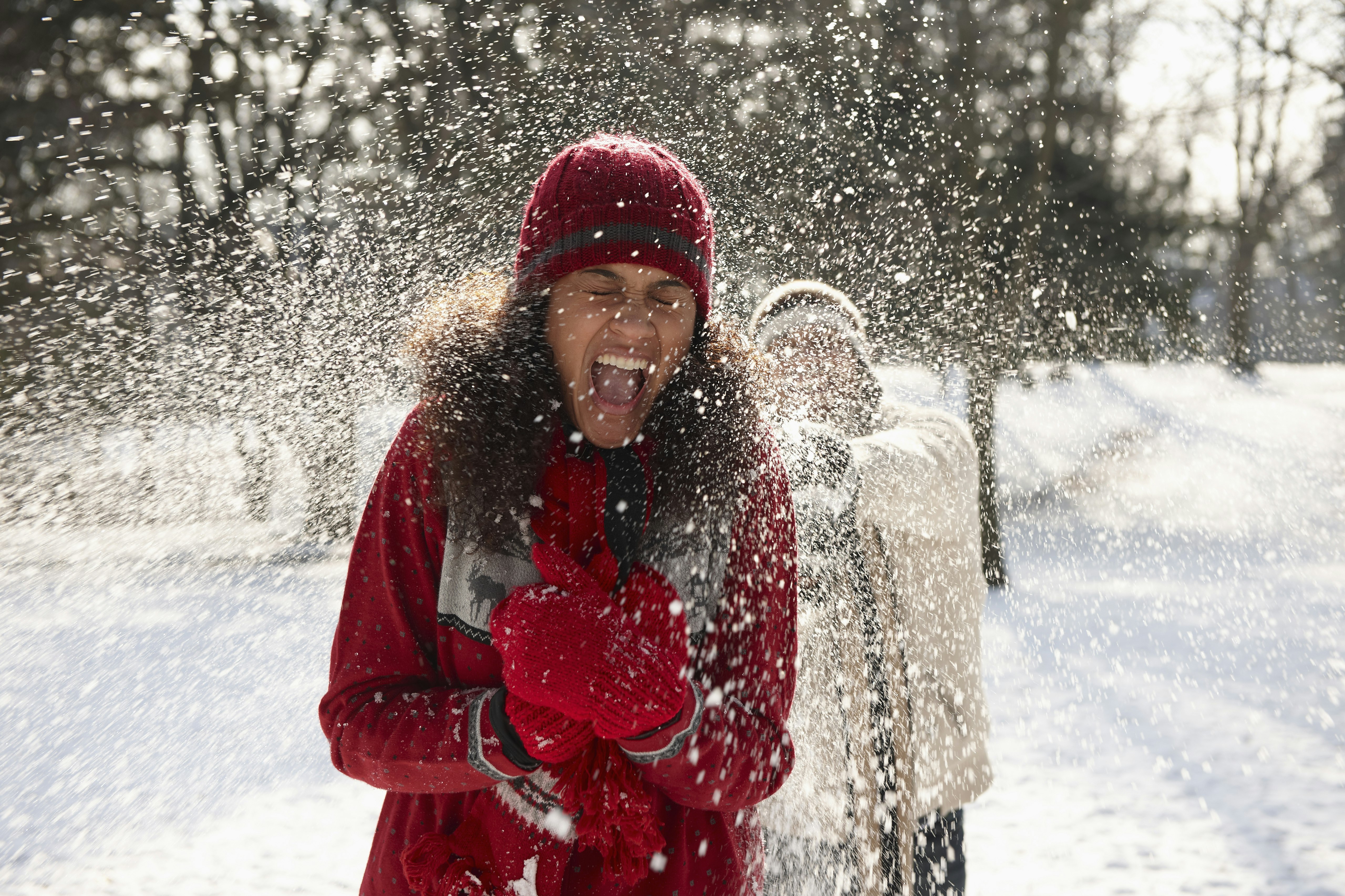 A woman wearing a bright red coat and hat, screams as she's hit with a snowball