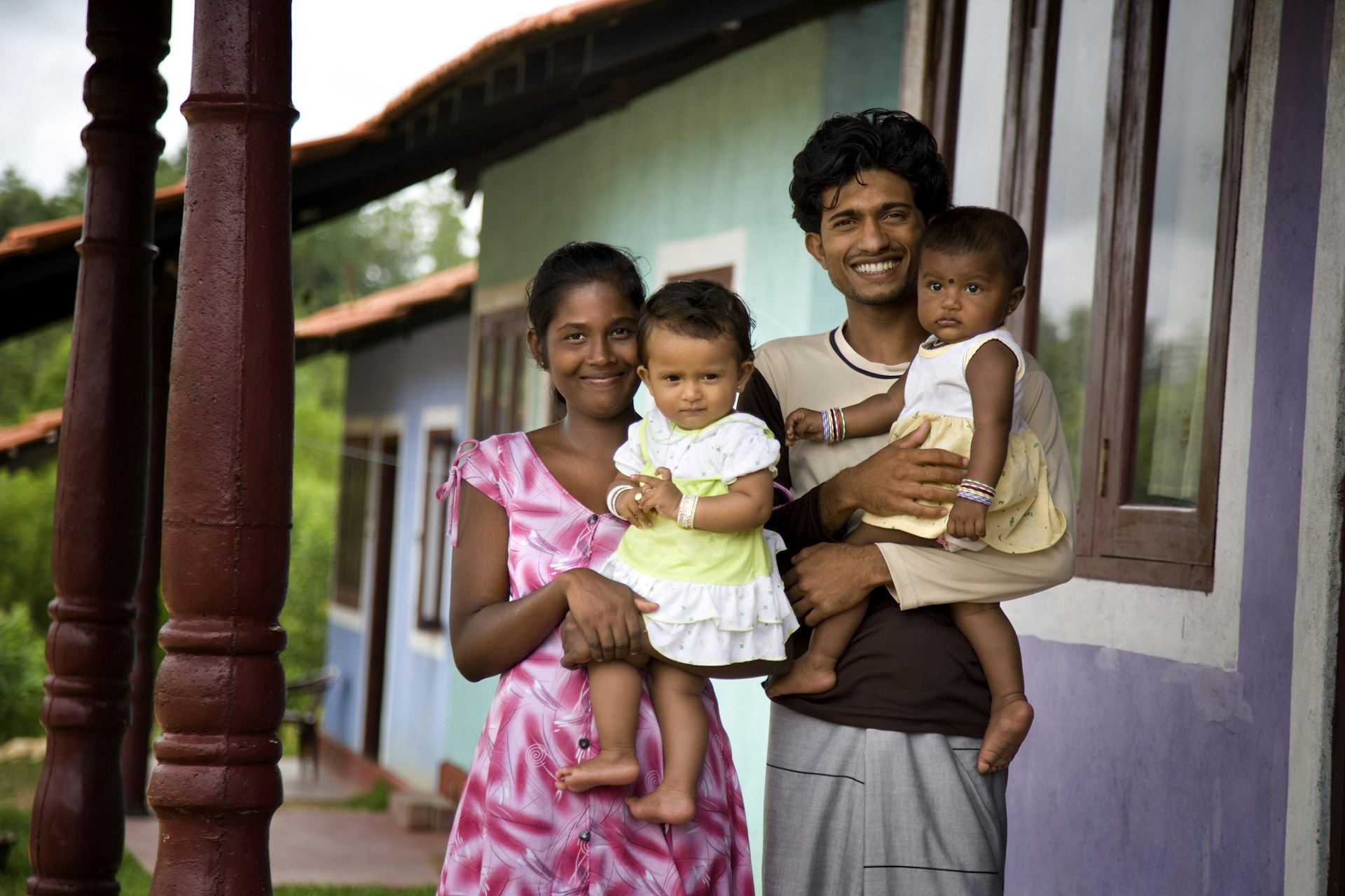 A Sri Lankan family of a woman, man, and two small babies. The adults are smiling into the camera