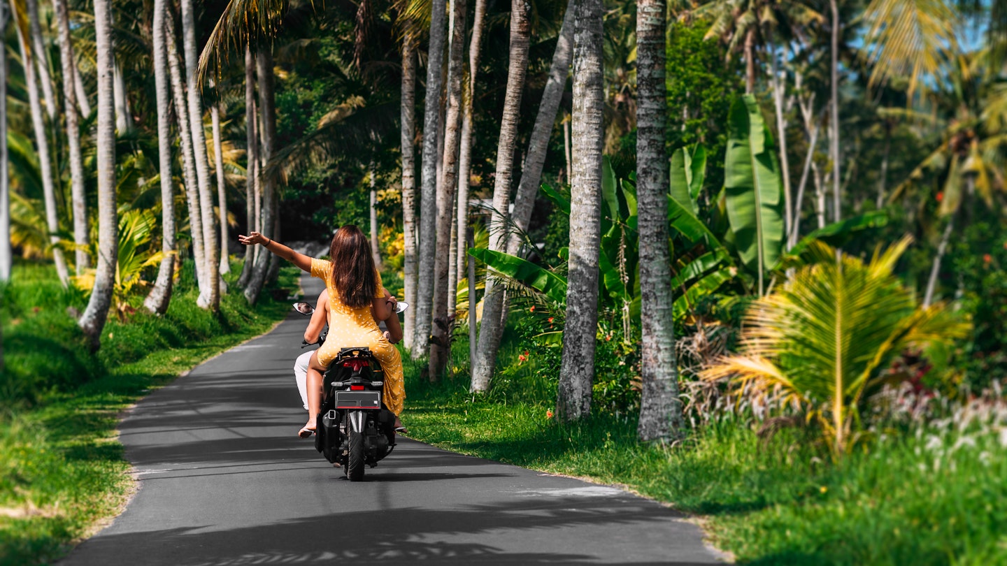 A happy young couple rides a scooter among the palm trees. A beautiful young couple is traveling on a scooter in Sri Lanka. Cheerful couple riding scooter at countryside road, vacation concept. ; Shutterstock ID 1937259352; your: Claire Naylor; gl: 65050; netsuite: Online editorial; full: Sri Lanka budget