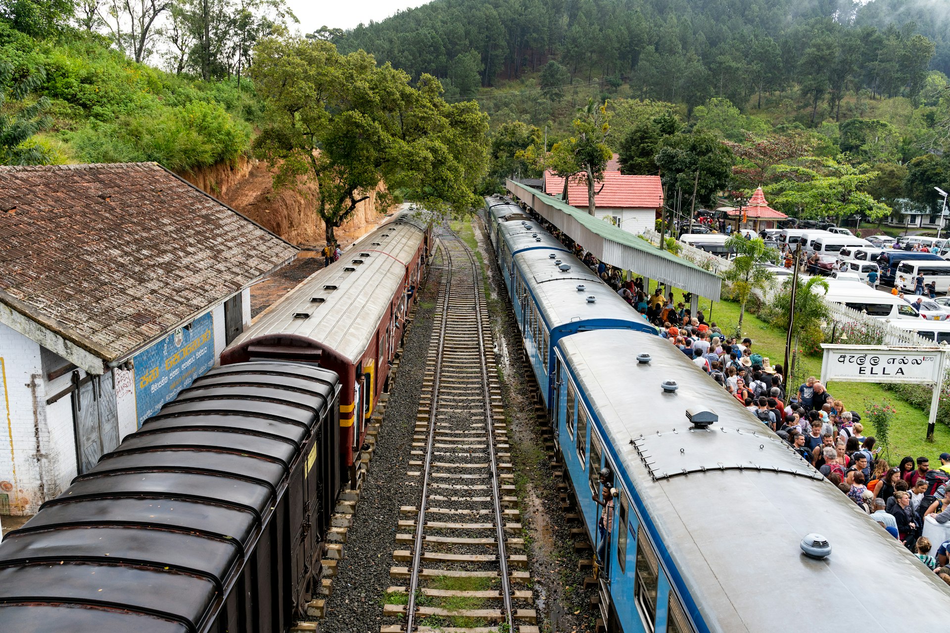 An aerial shot of two trains at a station. The right-hand platform is packed with people