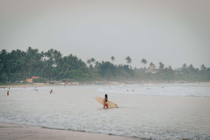 Surfers at Weligama beach in Sri Lanka on a hazy, rainy day
