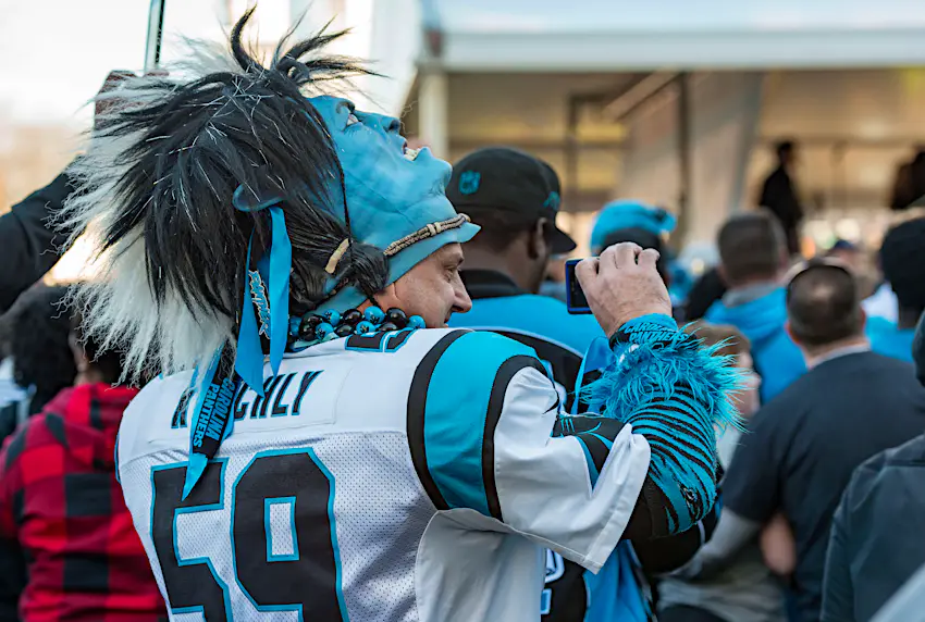 Going to a sporting event is a fun family activity in Charlotte; Closeup of a Carolina Panthers football fan, wearing a jersey and a mask pushed back on his head, taking a picture